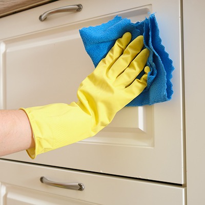 A person wearing a yellow rubber glove is cleaning a white cabinet door with a blue cloth.