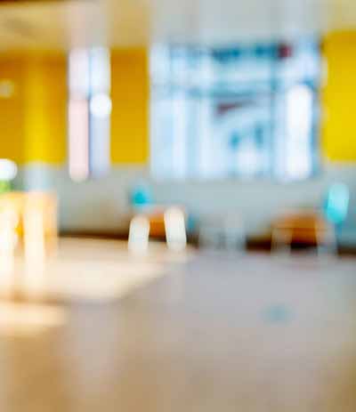 A brightly lit room with yellow walls and large windows, featuring blurred chairs and tables, creating an unfocused and abstract look.