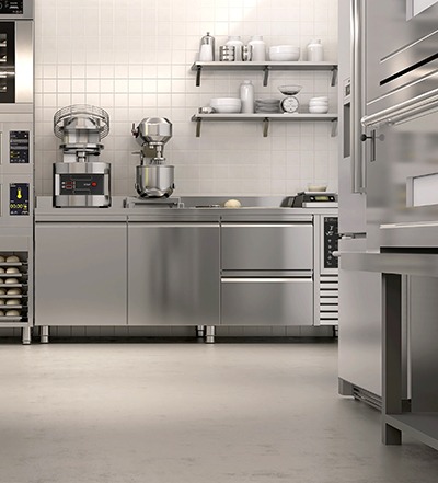 A modern commercial kitchen with stainless steel counters and appliances, two stand mixers, shelves with dishes and containers, and a clean, minimalist design.