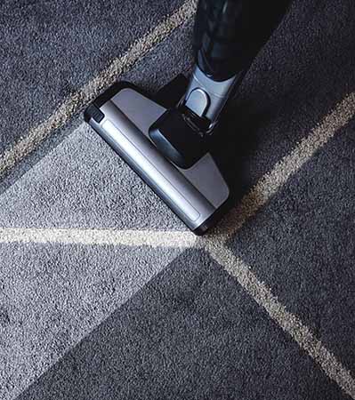 A vacuum cleaner is being pushed across a gray carpet with light and dark stripes, leaving a visibly clean path behind it.