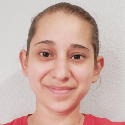 A person with light skin and brown hair pulled back is smiling softly at the camera, wearing a red shirt, against a plain light gray background.